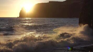 Sunset over the Scenic seascape with rocky shores silhoute. Big waves on golden warm water surface in motion blur with bokeh lights from sun. Holiday, vacation and recreational background concept video
