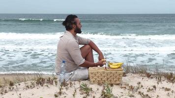 Man eating fruit and drinking water during picnic on the beach. Frontal Camera. video