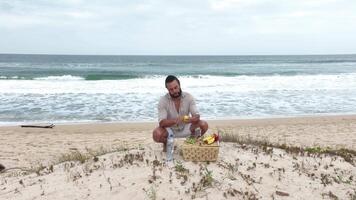 Man eating fruit and drinking water during picnic on the beach. Frontal Camera. video