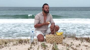 Man eating fruit and drinking water during picnic on the beach. Frontal Camera. video