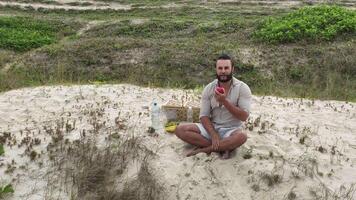Man eating fruit and drinking water during picnic on the beach. Frontal Camera. video
