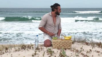 Man eating fruit and drinking water during picnic on the beach. Frontal Camera. video
