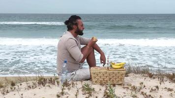Man eating fruit and drinking water during picnic on the beach. Frontal Camera. video
