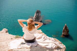 A woman is sitting on a rock overlooking the ocean. She is smiling and waving her hand in the air. The scene is peaceful and serene, with the ocean as the backdrop. photo