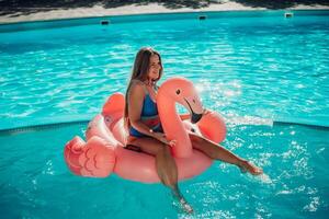 A woman is sitting on a pink inflatable flamingo in a pool. Concept of fun and relaxation, as the woman is enjoying her time in the water. photo