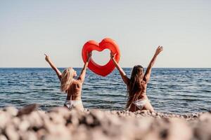 Two women are on a beach holding a heart shaped inflatable raft photo