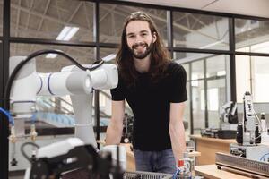 Portrait happy smile engineer male learning education in Industrial Robotics program with robot arm simulation model in university engineering lab classroom. photo