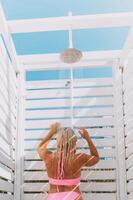 A woman in a bikini stands in front of a white shower stall. She is smiling and she is enjoying the moment. photo