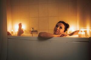 A woman is sitting in a bathtub with candles lit around her. She is smiling and she is enjoying her time. photo