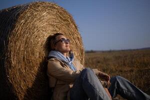 A woman is sitting in the middle of a hay bale, wearing sunglasses photo