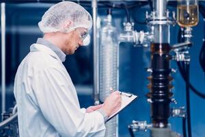 Scientist Medical Factory Staff Working in Science Lab. Medicine factory Technician Employee Check Care Products Quality in Sterilize Room Taking Note in Check list. photo