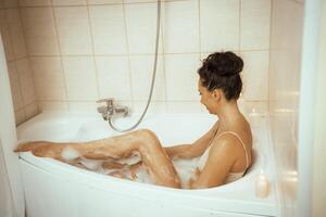A woman is sitting in a bathtub with bubbles and candles. She is smiling and she is enjoying her bath. photo