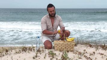 Man eating fruit and drinking water during picnic on the beach. Frontal Camera. video