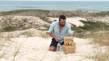 Man eating fruit and drinking water during picnic on the beach. Frontal Camera. video