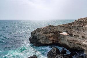A rocky cliff overlooks the ocean, with the water crashing against the rocks. The scene is serene and peaceful, with the sound of the waves providing a calming atmosphere. photo
