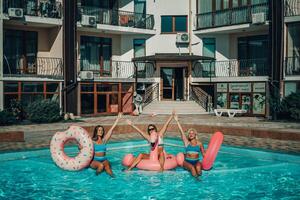 Three women are in a pool with inflatable toys, including a pink flamingo and a donut. photo