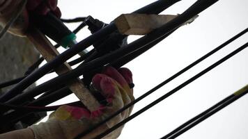 Skilled electrician fixes wires standing on ladder near high pole against blue sky on summer day backside view. Electrical service and mounting on the pole video
