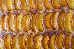 A close up of a dessert made of sliced peach. The dessert is covered in a caramel glaze and has a golden brown crust. The peach are arranged in a spiral pattern, creating a visually appealing photo
