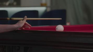 Close-up of the billiards player's hands as they strike the cue ball, which is positioned at the edge of the billiard table. Close up. Slow motion video