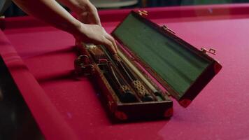 Woman takes out a valuable cue from a case to play American pool or snooker. Mid shot. Slow motion video