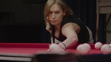 Portrait of a billiards player leaning over the table, aiming to strike the white ball. The player is focused and determined in her pursuit of the goal. Mid shot. Slow motion video