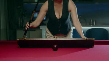 Woman in a bar prepares for an American pool game. She opens a case containing a professional pool cue and picks it up, while looking directly at the camera. Mid shot. Slow motion video