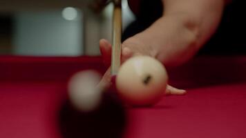 Close-up of a pool cue striking a white ball with the number six on a red pool table. Close up. Slow motion video