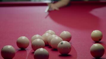 Triangle of billiard balls is disrupted by a powerful impact at the start of the game, causing them to fly in different directions across the red surface of the table. Close up. Slow motion video