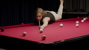 Woman leans over an unusual red pool table and strikes the ball with her cue, sending it into the pocket. video