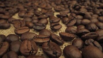 A close-up shot of roasted coffee beans scattered on a burlap surface. The beans are dark brown and shiny, with a deep, rich color. Coffee industry concept. Moving camera. video