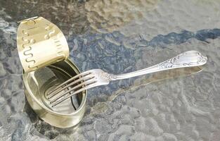 Open empty tin can and fork on the glass table surface photo