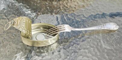 Open empty tin can and fork on the glass table surface. photo