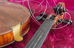 Broken violin and tangled strings, on a red background. photo