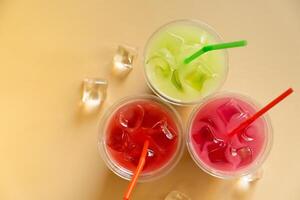 Colored summer lemonades on beige background with ice cubes photo