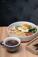 A bowl of couscous with meat, eggs and avocado, vegetables and a cup of coffee on the restaurant table photo