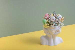 Plaster head statuette with Easter eggs and flowers. Easter creative concept photo