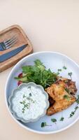 Delicious fried chicken wings with yogurt sauce and greens top view on beige background photo