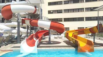 Colorful water slides at a resort water park, with red, orange, and yellow tubes leading into a refreshing pool. Sun loungers and umbrellas provide a relaxing atmosphere for a fun-filled summer day photo