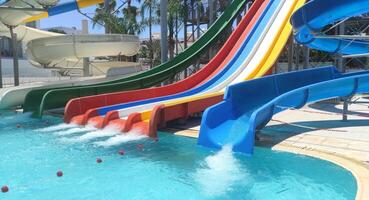 Sunny day at a lively water park with vibrant water slides and a splash pool. Surrounded by palm trees and under a clear blue sky, tropical vacation feel, ideal for family fun and excitement. photo