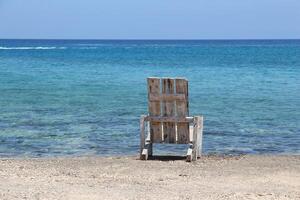 sereno playa escena con un rústico de madera silla frente a el claro azul mar, Perfecto para conceptos de relajación, soledad, y natural belleza. ideal para verano y viaje temas foto