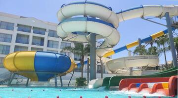 Bright summer day at a vibrant water park featuring colorful water slides and a splash pool. Palm trees and clear blue sky create a tropical vacation atmosphere, perfect for family fun and adventure photo