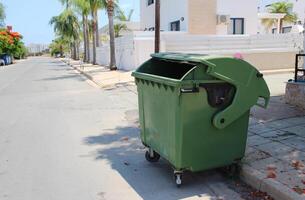 Green plastic trash container, trash can in the middle of the street. Reservoir for collecting, sorting and processing waste. Waste tank on a rotary on the street of Cyprus photo