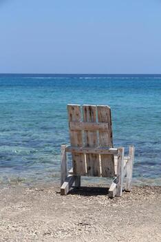 un tranquilo ver de el playa, un antiguo de madera silla y un cristal claro océano. para temas de paz, soledad y belleza de naturaleza, verano y viaje fotografía. vertical imagen foto