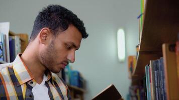 University Library. Talented Indian Boy Standing Next to Bookshelf Reads Book for His Class Assignment and Exam Preparations video