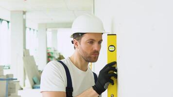 A man builder measures of the vertical deviation of plasterboard wall. Bubble level ruler close up view, measuring and leveling concept video