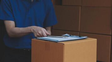 Young cheerful delivery man with parcel near car full of cardboard boxes, full length shot. Shipping service concept video