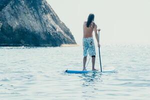 Man Sup Sea. Strong athletic man learns to paddle sup standing on board in open sea ocean on sunny day. Summer holiday vacation and travel concept. Aerial view. Slow motion photo