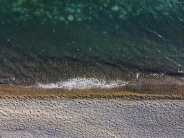 Aerial view from above on azure sea and pebbles beach. Small waves on cristal clear water surface in motion blur. Nature summer ocean sea beach background. Nobody. Holiday, vacation and travel concept photo