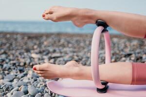 mujer mar pilates deportivo contento medio Envejecido mujer practicando aptitud en playa cerca mar, sonriente activo hembra formación con anillo en yoga estera afuera, disfrutando sano estilo de vida, armonía y meditación foto