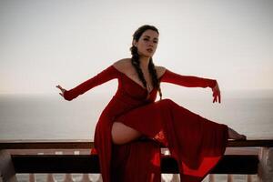 Closeup portrait of sensual young brunette woman in red dress, happily dancing outdoors isolated on blurry sea background with natural bokeh in soft warm sunset backlight. Selective focus. photo